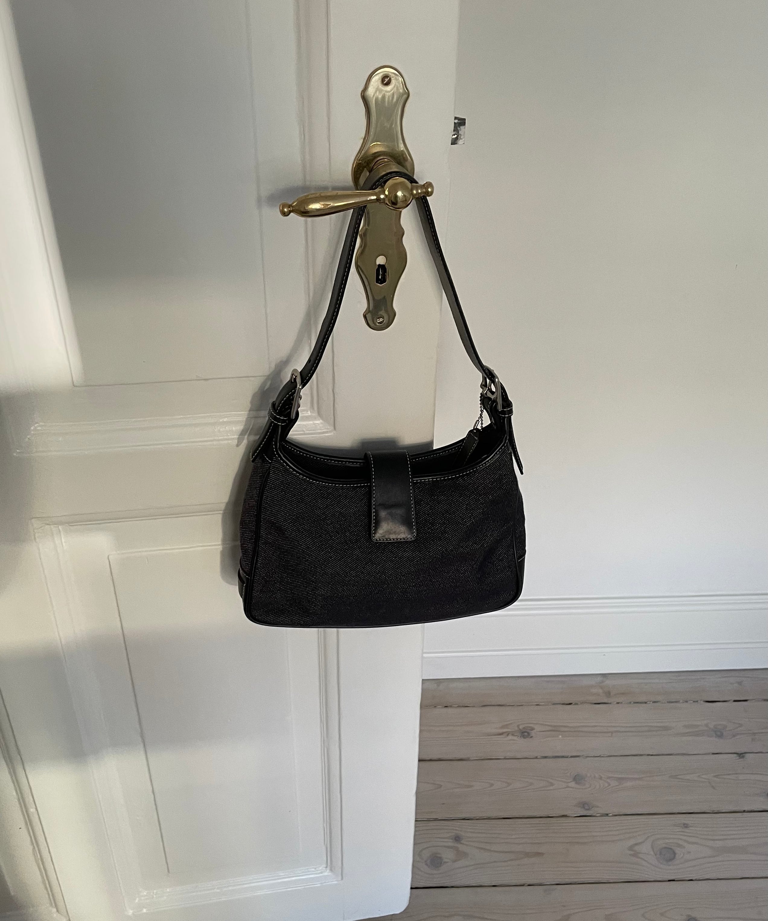 This vintage Coach bag from year 2000 is crafted from black leather and denim. It comes with an adjustable strap and magnetic closure, along with both an interior and exterior pocket. The bag is in great condition.