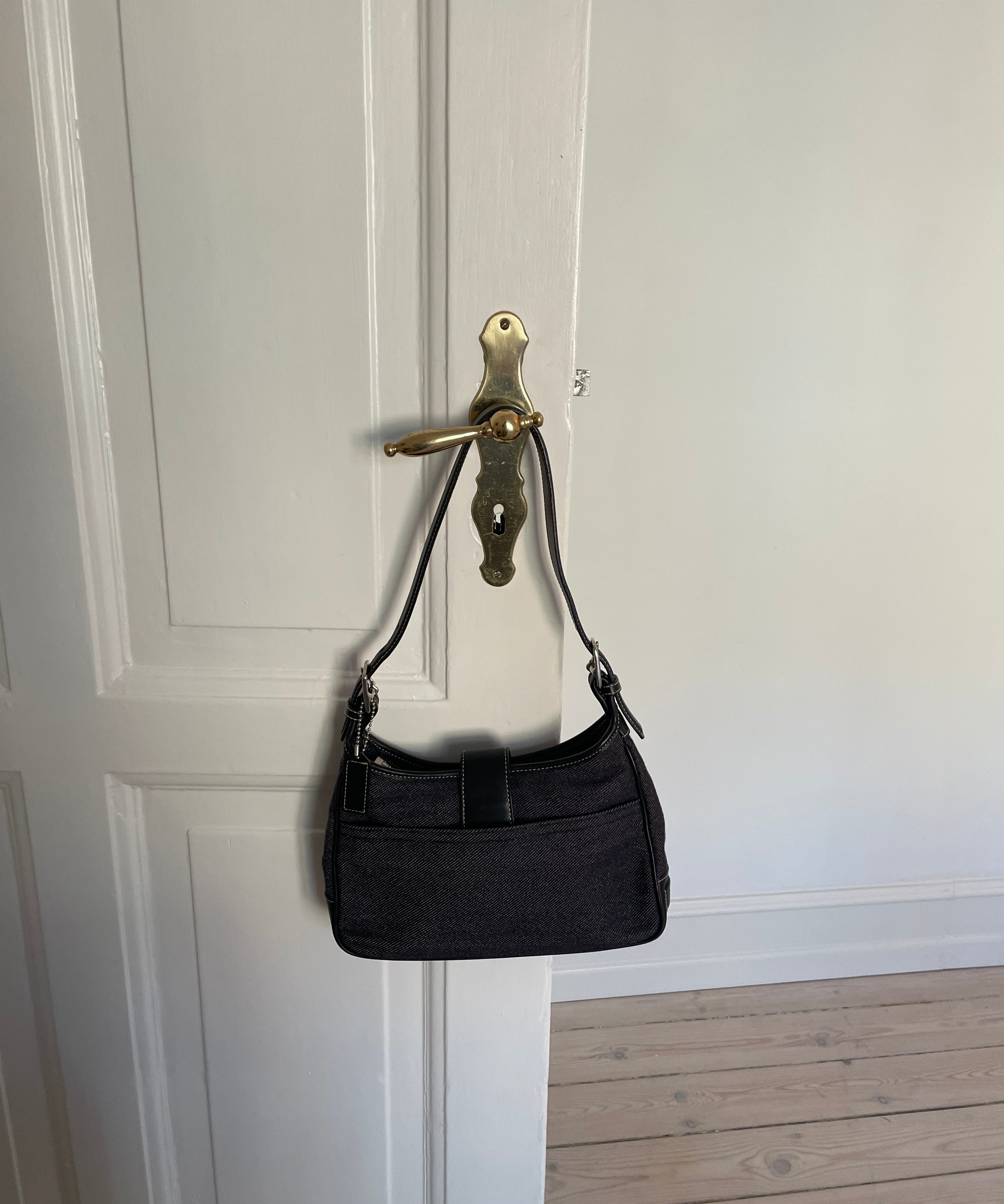 This vintage Coach bag from year 2000 is crafted from black leather and denim. It comes with an adjustable strap and magnetic closure, along with both an interior and exterior pocket. The bag is in great condition.